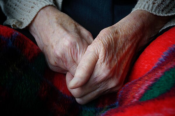 An elderly person's hands clasped together over a blanket